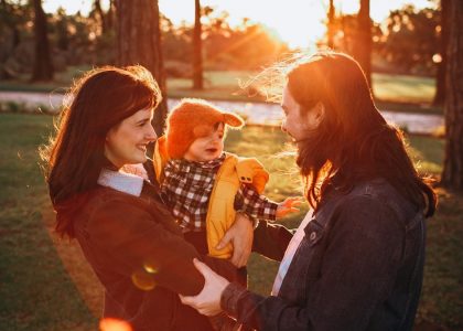 woman in black jacket carrying baby in white and black checkered dress shirt during daytime